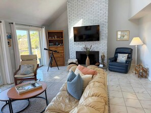 Una sala de estar con sofá, sillón, mesa, chimenea y televisor montado en una pared de ladrillo.