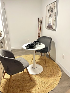 A dining area with a round table, two chairs, a woven rug, and a framed artwork on the wall. - Canal Private Suite - Welland (Welland)