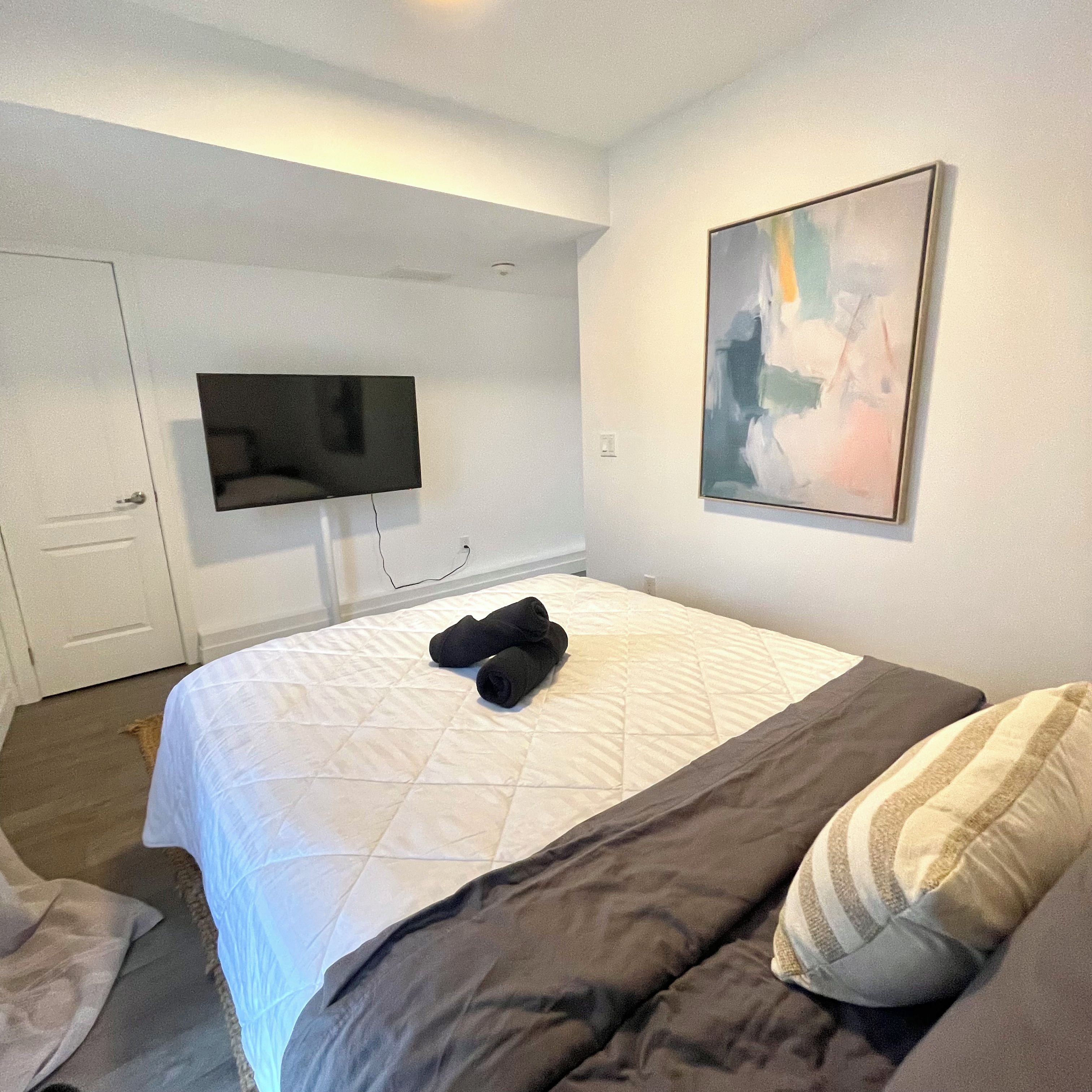 A hotel room with a bed, a television, and a painting on the wall.