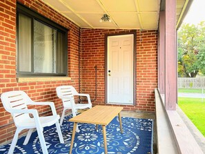A covered porch with a brick wall, a white door, and two white plastic chairs. - Comfort & convenience near Cleveland attractions! (Parma)