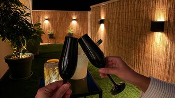 Twee personen met wijn glazen, een tafel met een kaars, en een bamboe wand met wandlampen.