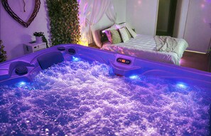 Ein Zimmer mit einem Bett, einer Wandpflanze und einer Jetted-Badewanne mit Blasen.