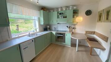 A kitchen with a dishwasher, a sink, a stove, and a dining area with a bench.