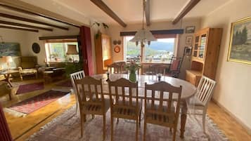 Un comedor con una mesa redonda y sillas, vigas de madera en el techo y vistas por la ventana.