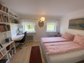 Une chambre avec deux lits, un bureau, une chaise, un radiateur et une bibliothèque.