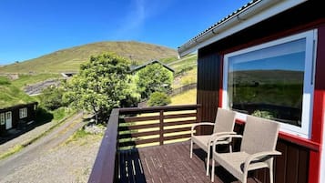 Een houten terras met twee rieten stoelen en een groot raam met uitzicht op een groen landschap.