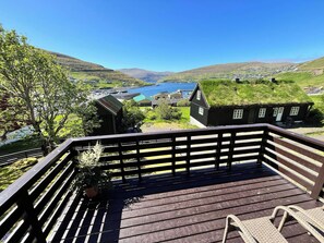 A wooden deck with a railing overlooking a village with traditional houses and a body of water.