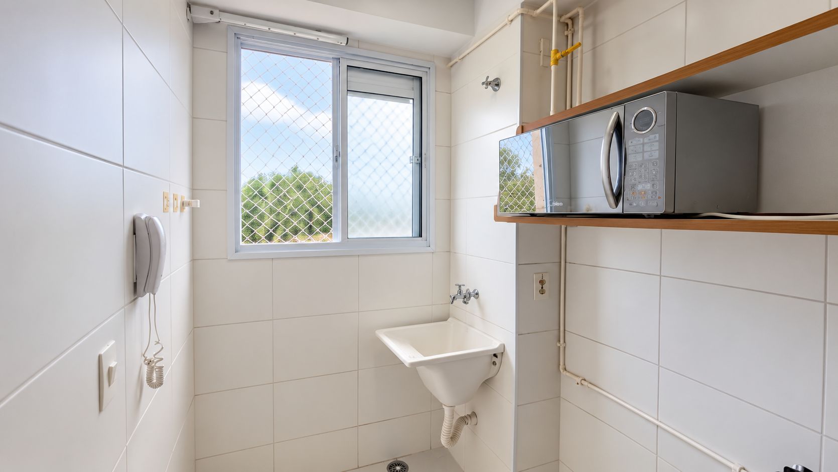 Une salle de bain avec une fenêtre, un lavabo, des toilettes et un lave-linge posé sur une étagère.