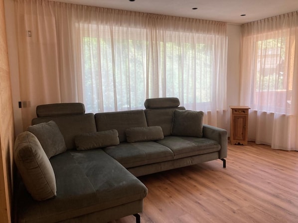Un sofà modular en una habitació amb sòl de fusta i grans finestres amb cortines translúcides.