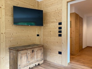 Una habitació amb parets de fusta, televisió penjada a la paret, un armari de fusta i una porta que dona a una altra habitació.