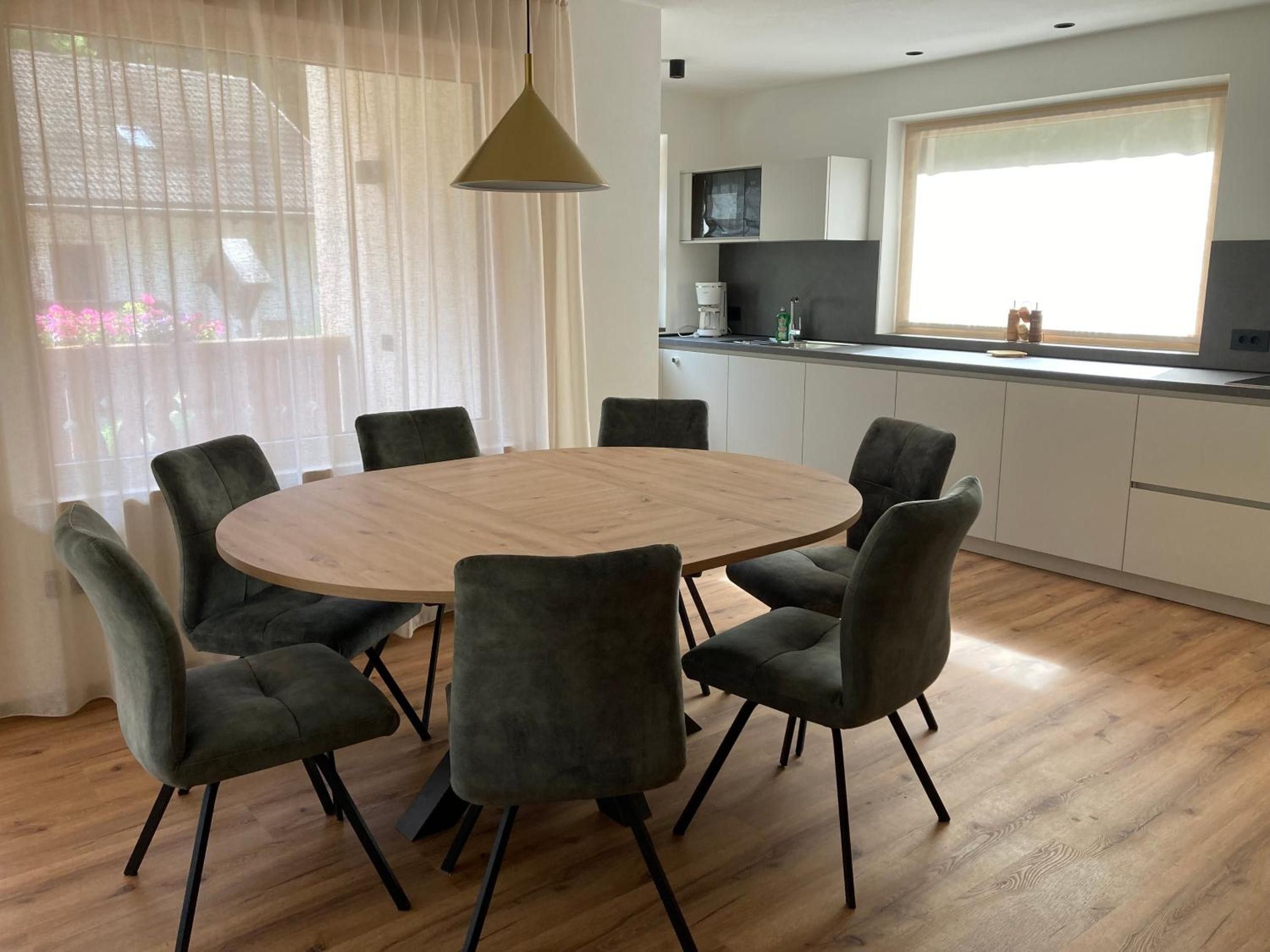 A modern kitchen with white cabinets, a round wooden table, and six grey chairs.