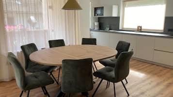 A modern kitchen with white cabinets, a round wooden table, and six grey chairs.