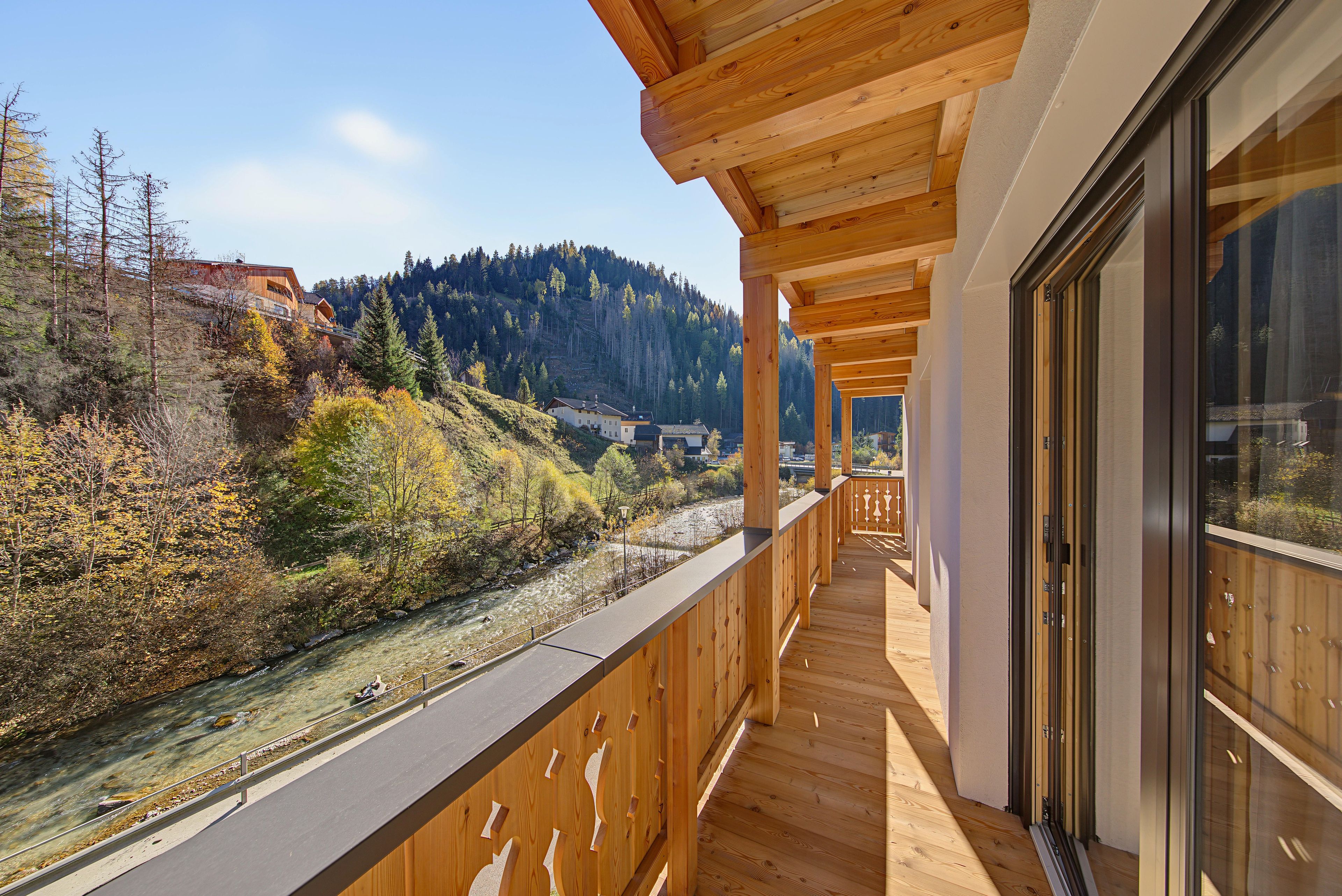 Un balcon en bois offrant une vue sur une rivière et des collines boisées.