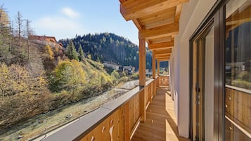 Un balcon en bois offrant une vue sur une rivière et des collines boisées.