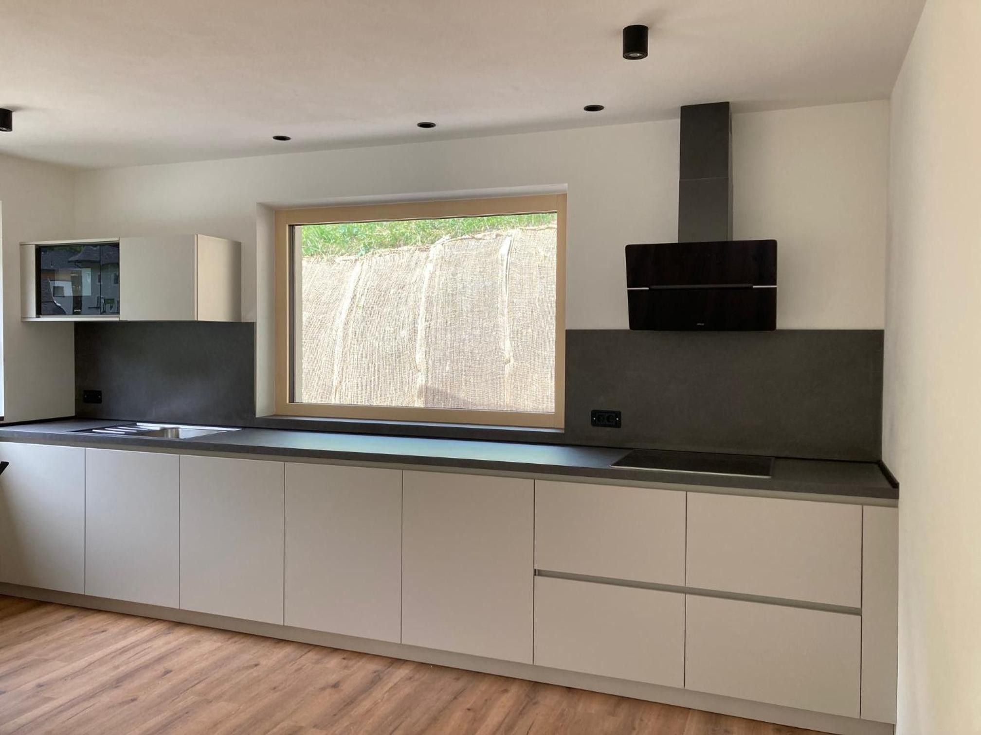 Une cuisine moderne dotée d’une fenêtre intégrée, d’une hotte noire et d’un design minimaliste.