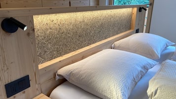 Una cama litera de madera con cabecera de listones y una ventana con vistas a la vegetación.