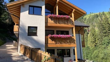 A two-story building with wooden balconies, a gravel driveway, and a mountainous backdrop.