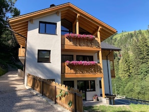 A two-story building with wooden balconies, a gravel driveway, and a mountainous backdrop. - Apartment 'Pe De Munt Mez Col' with Mountain View, Balcony and Wi-Fi (La Valle)