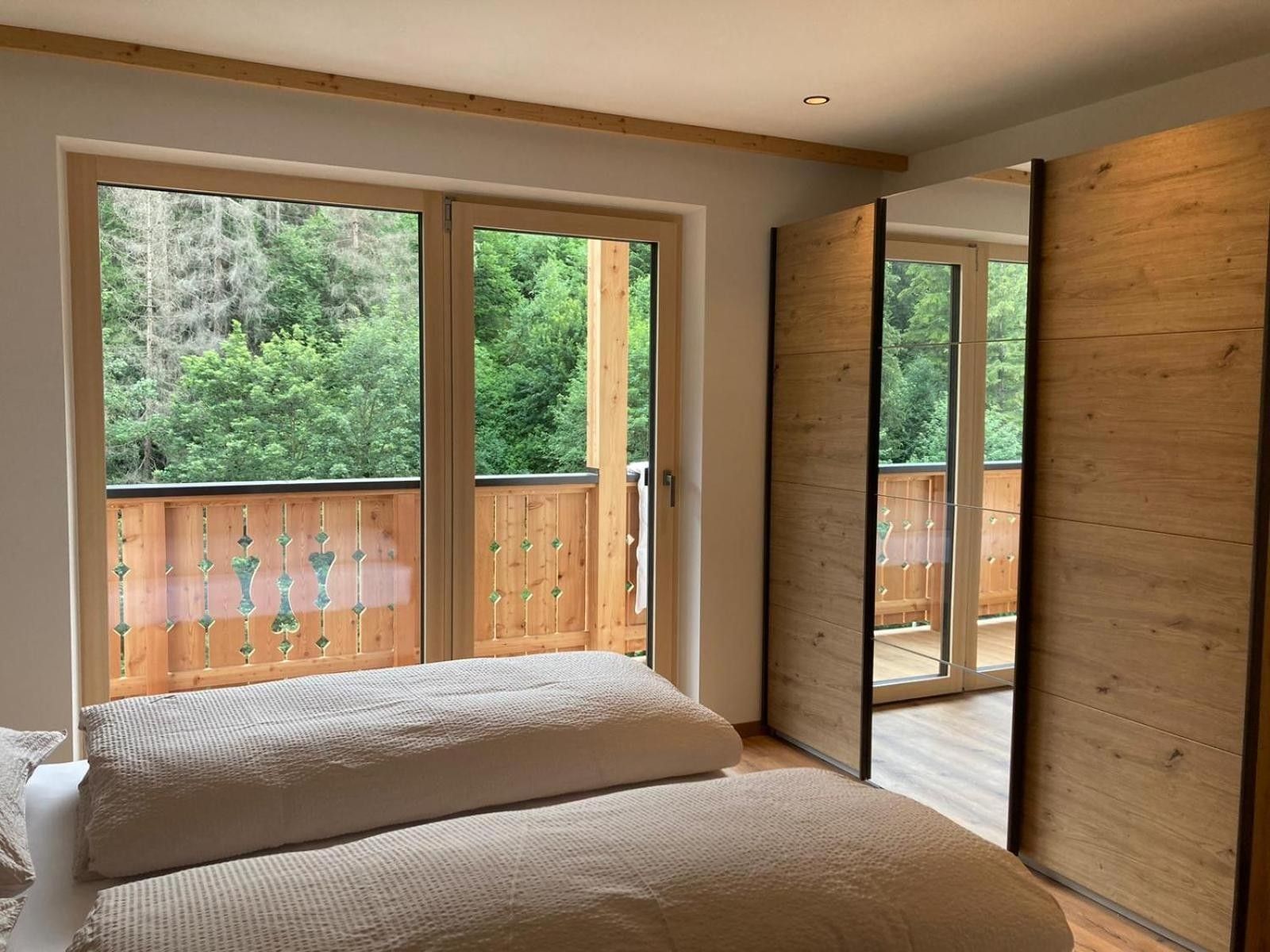 Un dormitorio con una cama grande, dos ventanas y vistas a una terraza de madera y árboles.