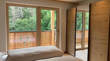 Un dormitorio con una cama grande, dos ventanas y vistas a una terraza de madera y árboles.