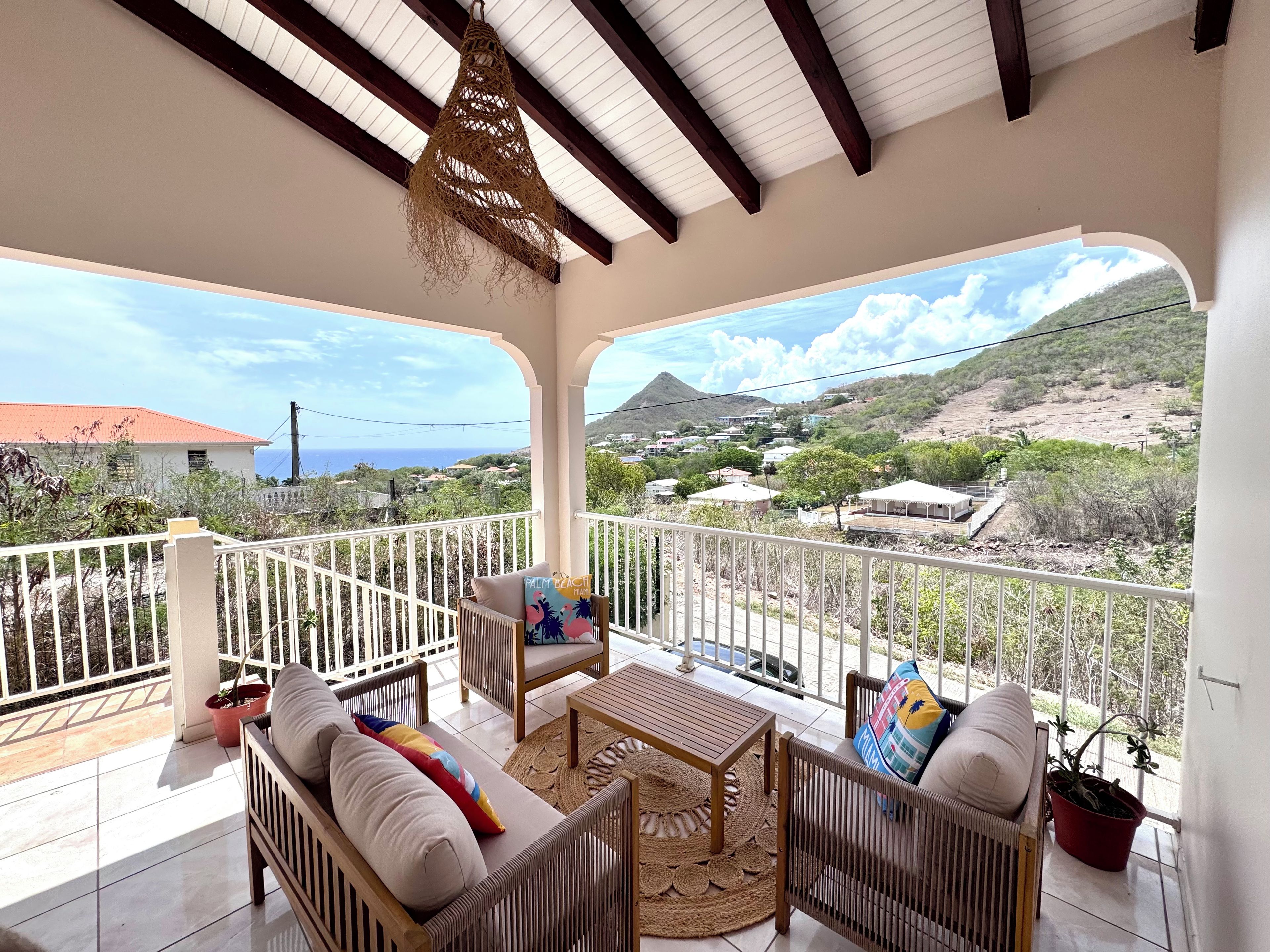 A covered balcony with wicker furniture, a view of a mountainous landscape, and a clear sky.