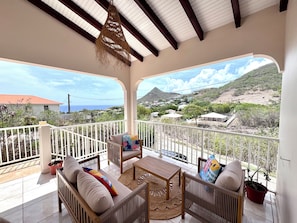 A covered balcony with wicker furniture, a view of a mountainous landscape, and a clear sky. - Villa Between Land and Sea (Les Anses-d'Arlet)