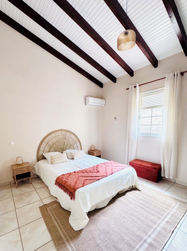 A bedroom with a bed, a red bench, a window with curtains, and a ceiling fan. - Villa Between Land and Sea (Les Anses-d'Arlet)