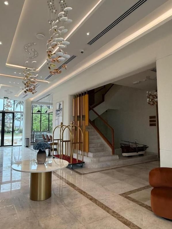 A spacious lobby with a marble floor, a round table with a vase, a staircase, and a boat model.
