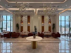 A modern lobby with sofas arranged in a U-shape, a central round table, and decorative hanging lights. - Al Montazah Park Hotel Suites (Salalah)