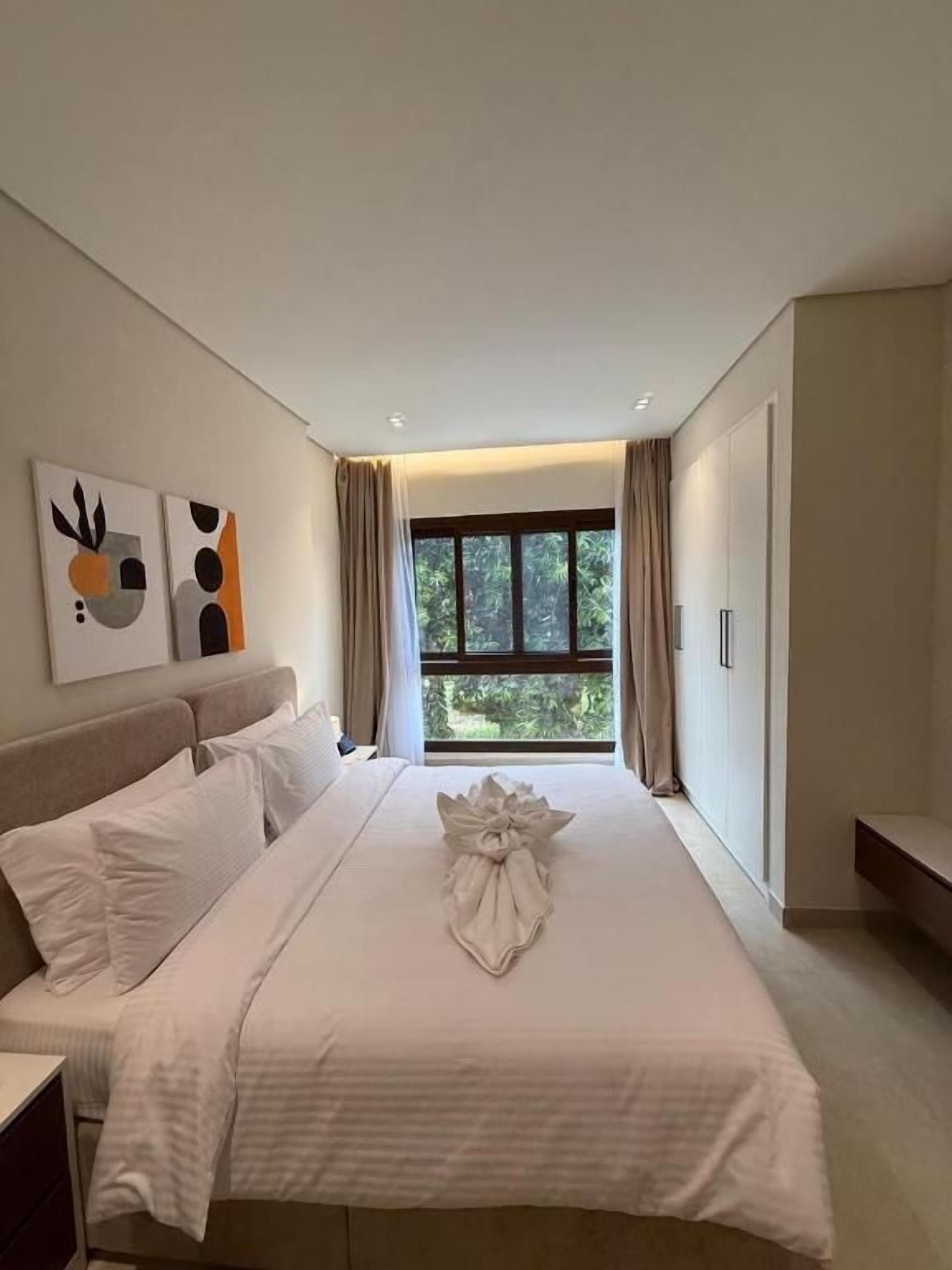 A hotel room with a large bed, a bedside table, a window with curtains, and artwork on the wall.