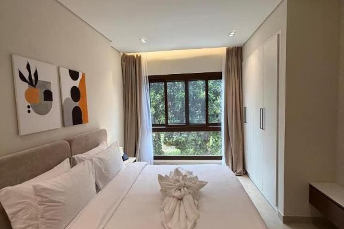 A hotel room with a large bed, a bedside table, a window with curtains, and artwork on the wall.