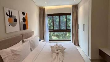 A hotel room with a large bed, a bedside table, a window with curtains, and artwork on the wall.