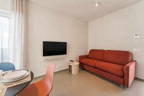 A modern living room with a flat-screen TV mounted on the wall, a red sofa, a small round table with a glass of wine, and a dining area with a table and chairs. - Oltrevista Terrace By the Sea (Monopoli)