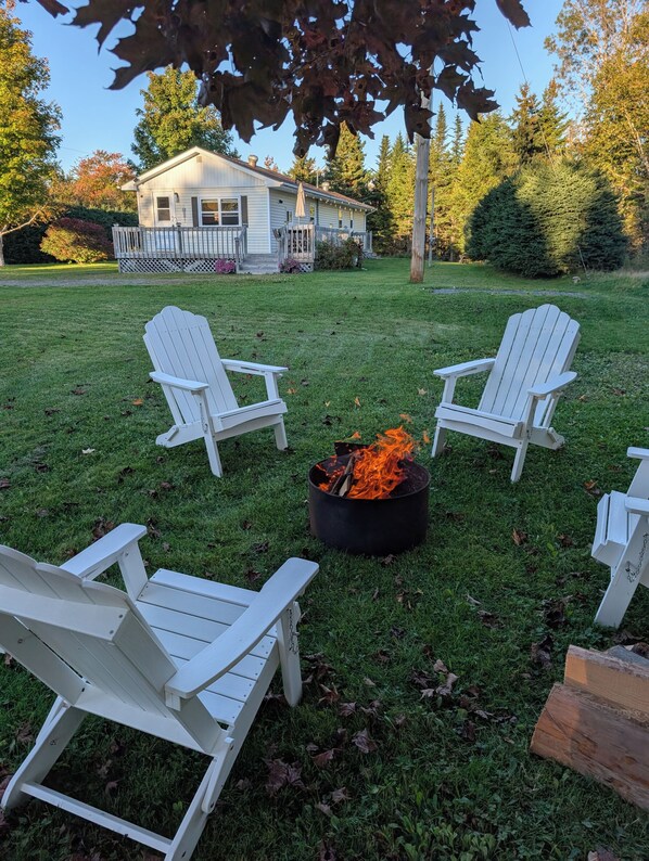 A backyard with a fire pit and Adirondack chairs.