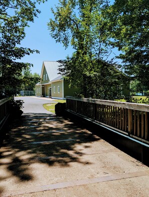 A pathway leading to a building with a green facade and a sloped roof, surrounded by trees. - Carmella Cottage, Antigonish (Antigonish)