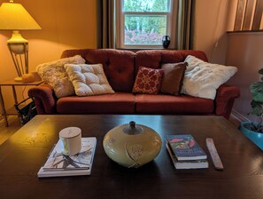 A cozy living room with a red sofa, a wooden coffee table, and a window with a view of trees.