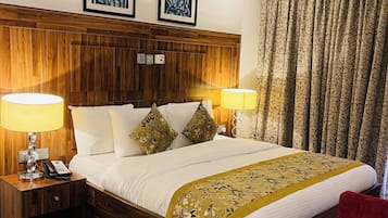 Quarto de hotel com cabeceira de madeira, duas luminárias de apoio, telefone, cama com roupa branca e manta floral, e uma cadeira vermelha.