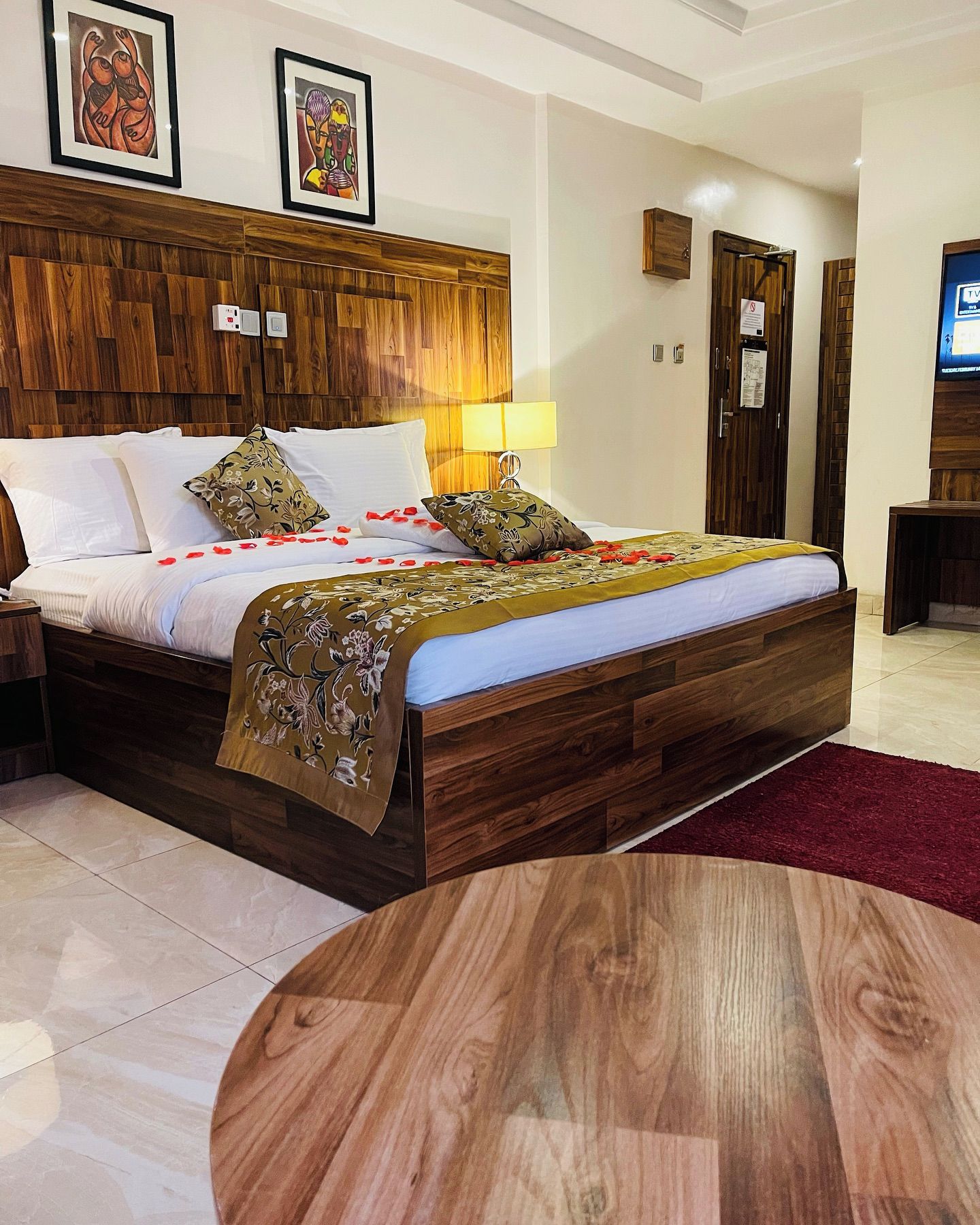A hotel room with a wooden bed, a round table, and a TV on the wall.