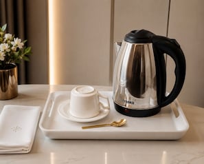 Una bandeja blanca con una cafetera, una taza y una cuchara sobre una superficie de mármol.