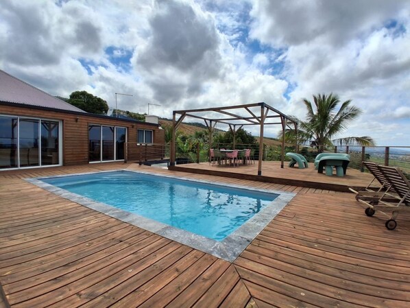 Une terrasse en bois avec une piscine, du mobilier d’extérieur et une pergola.