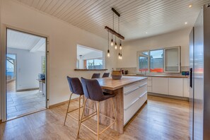 A modern kitchen with a wooden island, bar stools, and pendant lighting. - Villa Galéa - Climatisée, vue mer, piscine (Etang-Salé les Hauts)