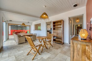A spacious living area with a dining table, wicker chairs, and a wooden cabinet. - Villa Galéa - Climatisée, vue mer, piscine (Etang-Salé les Hauts)