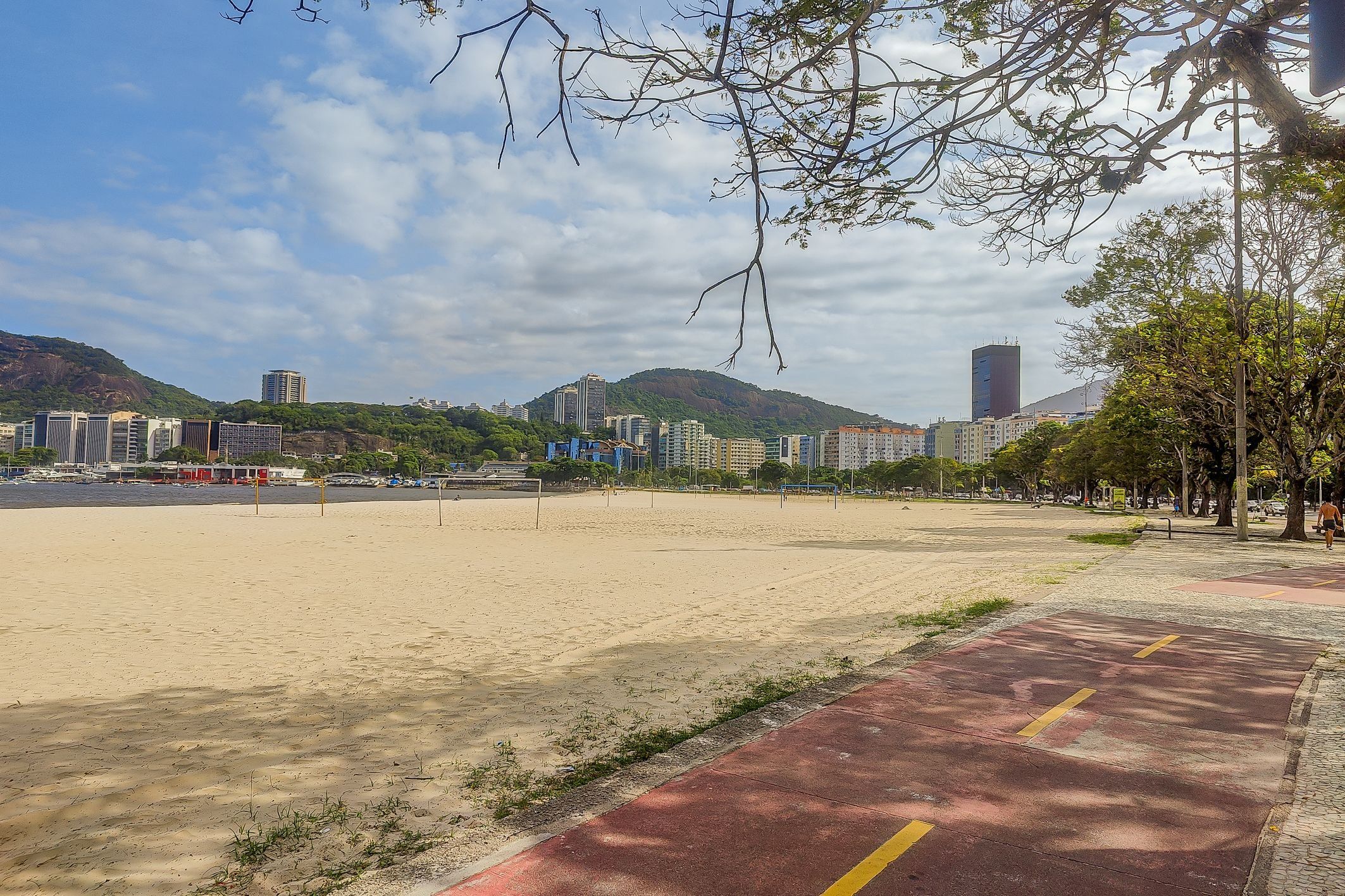 Uma praia com um caminho vermelho, edifícios ao fundo e um céu claro.