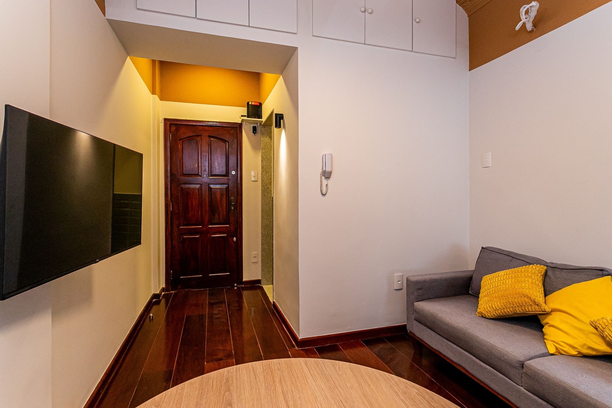 Una sala de estar moderna con un televisor de pantalla plana, un sofá gris con cojines amarillos y piso de madera.