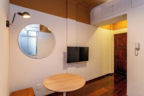 Un pasillo con un espejo redondo, un televisor de pantalla plana y una mesa de madera.