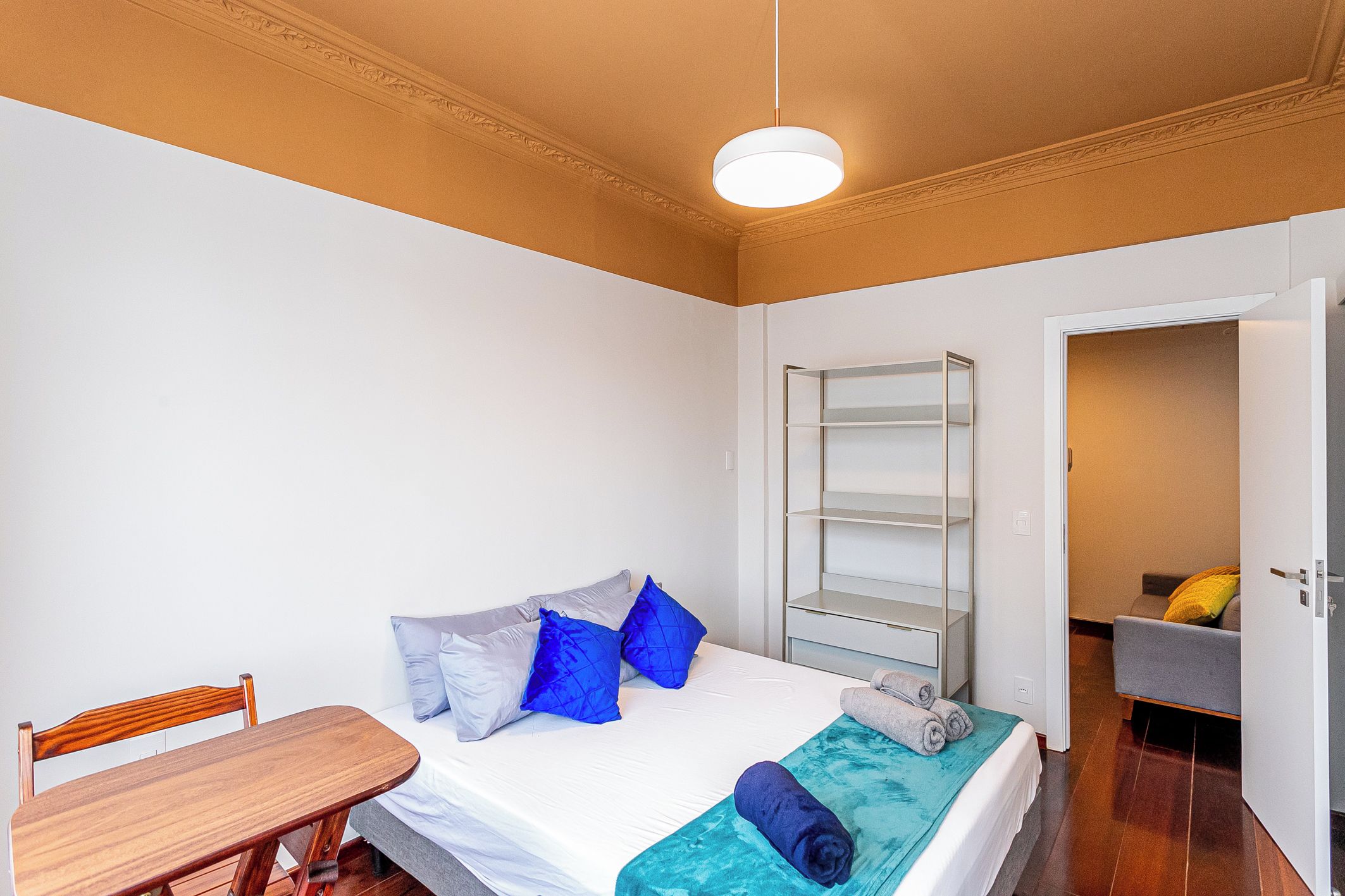 A bedroom with a bed, a wooden chair, a wardrobe, and a bathroom visible through an open door.