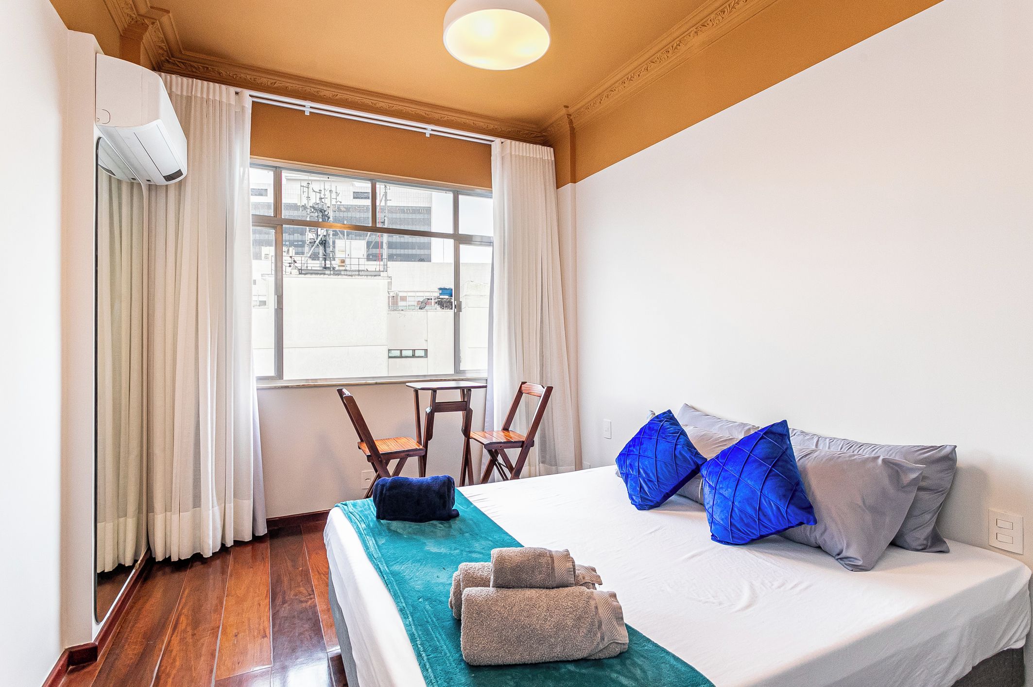 A hotel room with a bed, two chairs, a window with curtains, and a ceiling light.