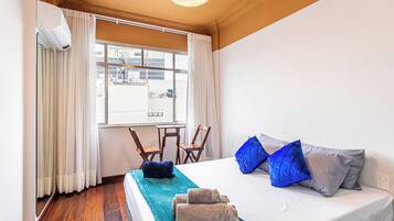 A hotel room with a bed, two chairs, a window with curtains, and a ceiling light.