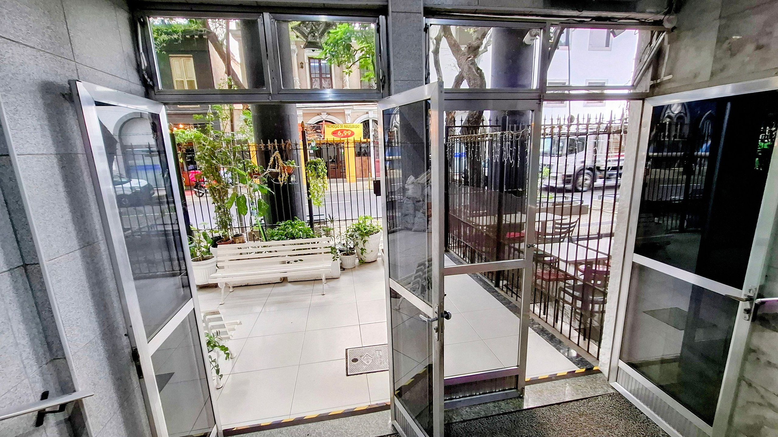Entrada de hotel con puerta de cristal, un banco exterior y plantas en macetas.