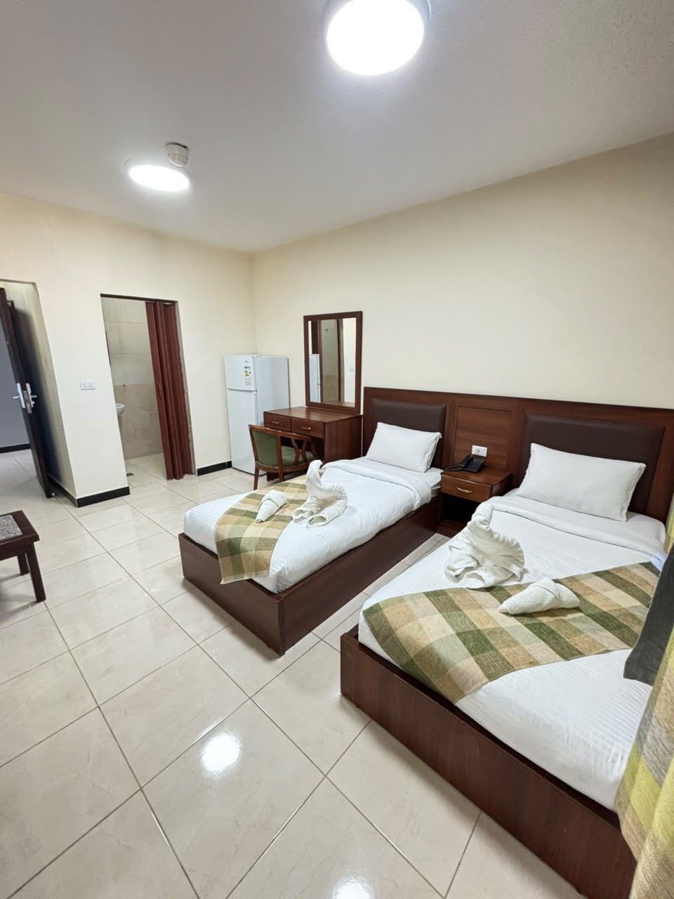 Habitación de hotel con dos camas, un escritorio, una silla, un espejo y un refrigerador.